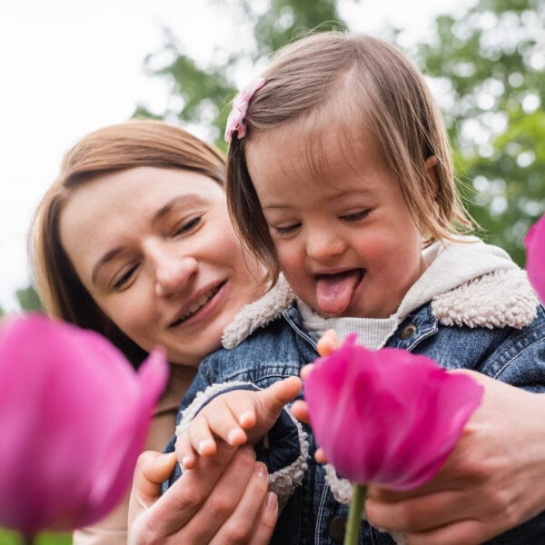 child with mental disability sticking out tongue near mother and blurred flowers